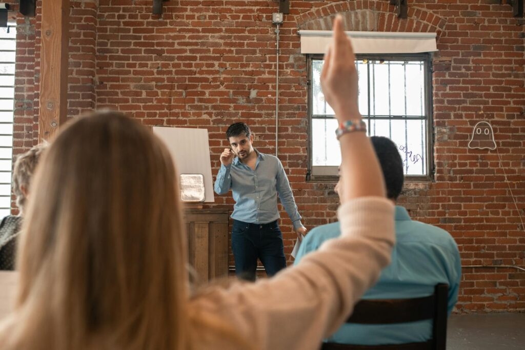 Teacher engaging with students in a classroom setting, encouraging participation. Project Manager Degree